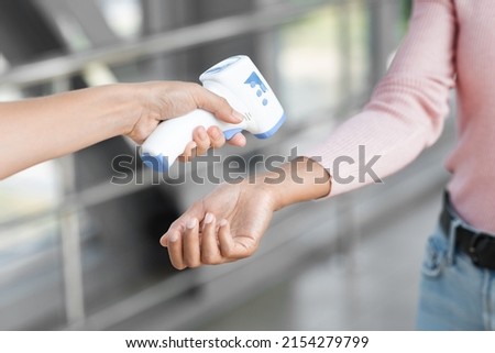 Temperature Control. Closeup Shot Of Security Stuff Member Using Electronic Medical Thermometer To Female At Airport Entrance, Passenger Woman Giving Her Wrist For Measuring During Covid-19 Foto stock © 