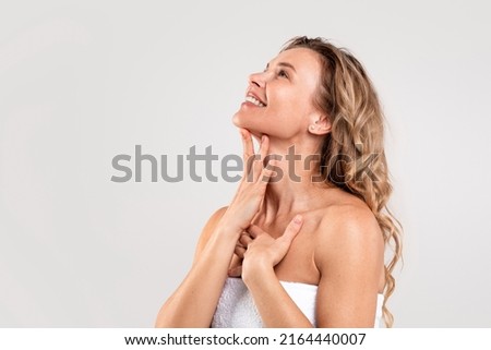 Photo of Double Chin Treatment. Beautiful Middle Aged Woman Touching Soft Smooth Skin On Neck, Attractive Mature Lady Standing Wrapped In Towel Over Light Grey Background, Enjoying Her Beauty, Copy Space