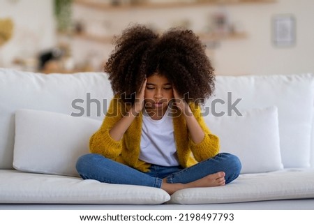 Stressed  preteen girl with bushy hair sitting on couch at home, touching her head, looking doen, copy space. Unhappy child suffering from loneliness while COVID-19 pandemic Stockfoto © 