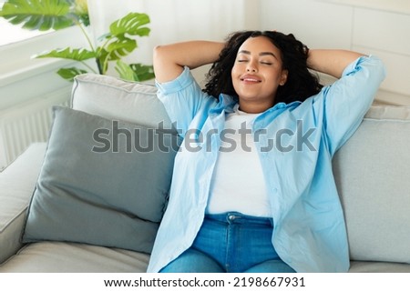 Relaxed African American Female Resting With Eyes Closed Sitting On Couch At Home. Woman Enjoying Weekend And Domestic Comfort In Modern Living Room Indoor Photo stock © 