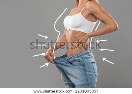 Young Slim Female Pulling Big Jeans And Showing Result Of Weight Loss With Drawn Silhouette Outlines And Arrows, Unrecognizable Sporty Woman In Oversized Clothes Demonstrating Body After Slimming Foto stock © 
