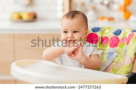 Similar – Image, Stock Photo Baby seated in high chair reaching for spoon; dramatic natural lighting and messy tray table