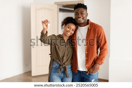 Real Estate. Cheerful African American Spouses Showing New House Key Smiling To Camera, Embracing Standing Among Moving Cardboard Boxes At Home. Relocation, Apartment Ownership And Family Housing