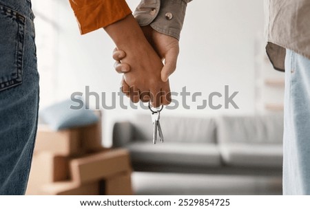 Closeup of young couple holding hands and new house key, moving in together. Unrecognizable boyfriend and girlfriend relocating to their own property, cropped view. Mortgage, real estate concept