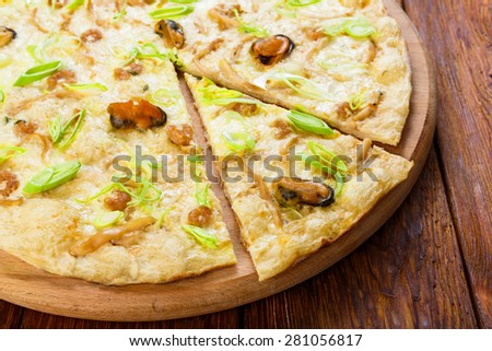 Delicious seafood pizza with shrimps, mussel, olives and leek - thin pastry crust at wooden table background