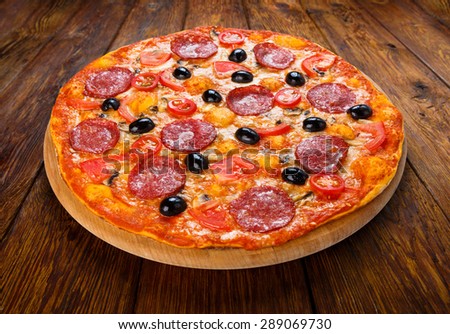Delicious italian pizza with salami pepperoni, mushrooms and black olives - thin pastry crust at wooden table background