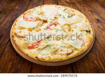 Delicious pizza with chicken, parmesan, tomatoes, white sauce and fresh arugula - thin pastry crust isolated at wooden background, above view