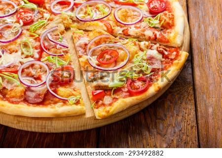 Delicious pizza with fresh onions, leek, bacon and cherry tomatoes - thin pastry crust isolated at wooden background on wooden desk