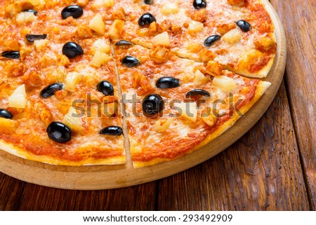 Delicious italian pizza with pineapple, chicken and black olives - thin pastry crust at wooden table background on wooden desk