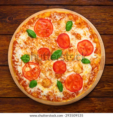 Delicious italian Margherita pizza with tomatoes and mozarella - thin pastry crust at wooden table background, above view on wooden desk