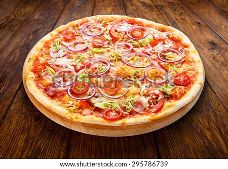 Delicious pizza with fresh onions, leek, bacon and cherry tomatoes - thin pastry crust isolated at wooden background on wooden desk