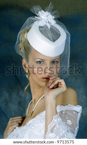 Portrait of the smiling blonde in white wedding dress and hat with veil. Studio photo