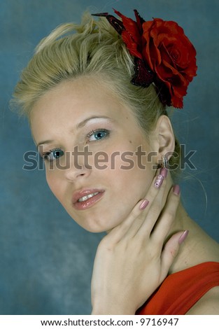 Portrait of the smiling blonde in red dress and with red flower in hair. Studio photo