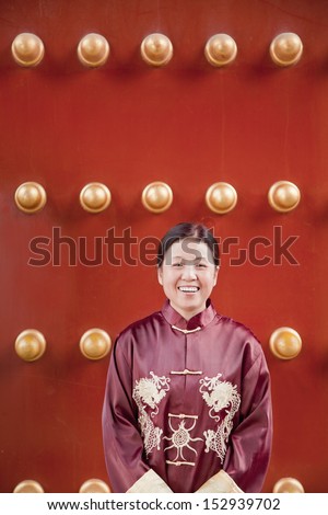 Mature woman in traditional clothes standing next to traditional Chinese door