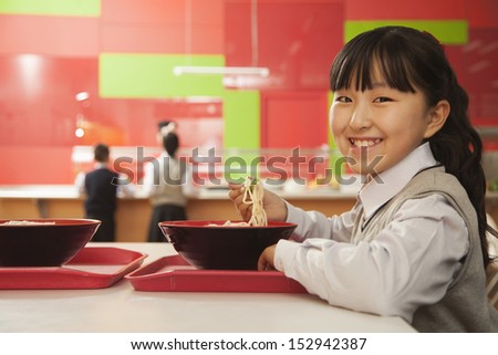 School girl eats noodles in school cafeteria