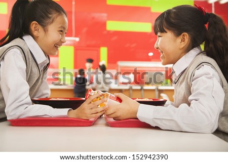 Two school girls talk over lunch in school cafeteria