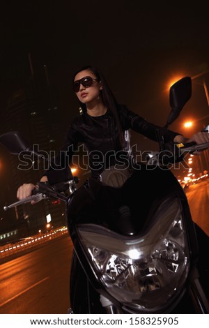 Beautiful young woman riding motorcycle in sunglasses at night
