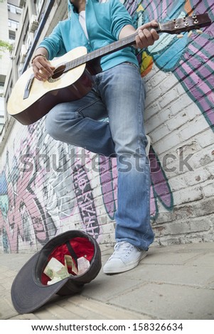 Young street musician playing guitar and busking for money