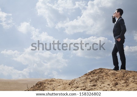 Young businessman in sunglasses standing in the desert and talking on phone
