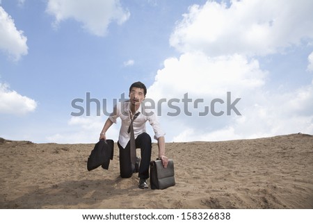 Young businessman kneeling in the desert and holding a briefcase