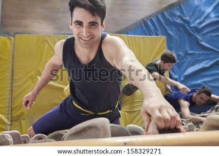 Smiling young man climbing up a climbing wall