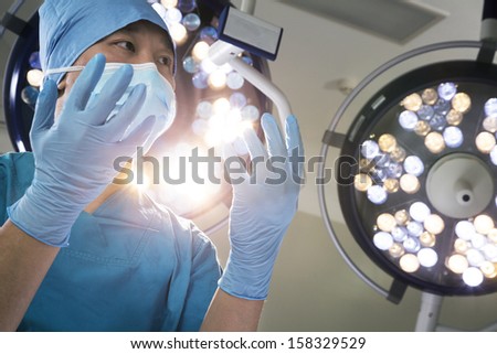 Low angle view of surgeon holding gloved hands up with surgical lights behind him
