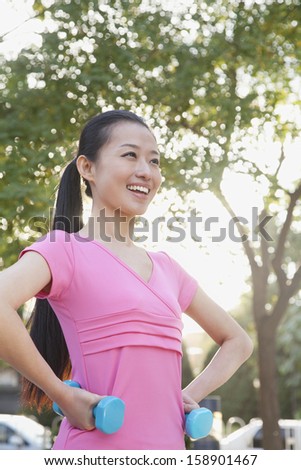 Young woman exercising in park with dumbbells