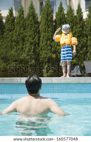 Portrait of son with snorkeling equipment standing by pool as father waits in water