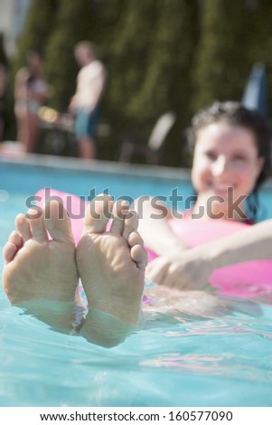 Young woman in pool holding onto inflatable raft with feet sticking out of water