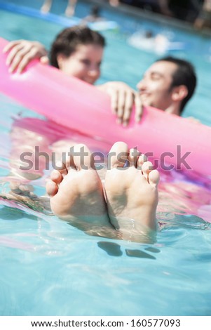 Two friends in pool holding onto inflatable raft with feet sticking out of water