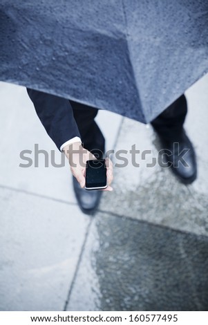 High angle view of businessman holding umbrella and looking at his phone in the rain