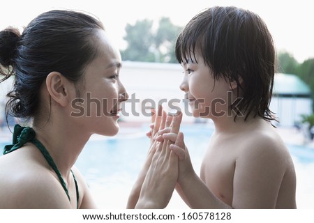Smiling mother and son face to face and holding hands by the pool