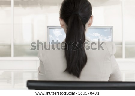 Businesswoman sitting in front of computer with clouds and sky on monitor