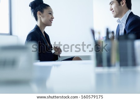 Two colleges smiling and talking by desk in office