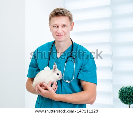 Young cute doctor veterenarii in the green uniform with a rabbit in his hands