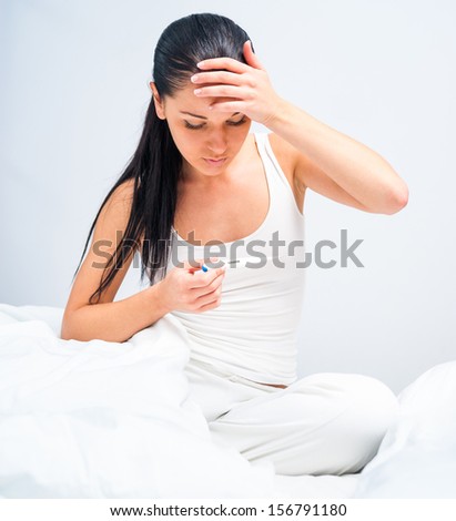 brunette measures the temperature of a sick in bed