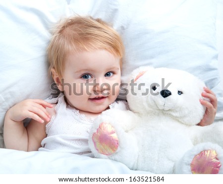 cute baby lying in white bed and holding a teddy bear toy