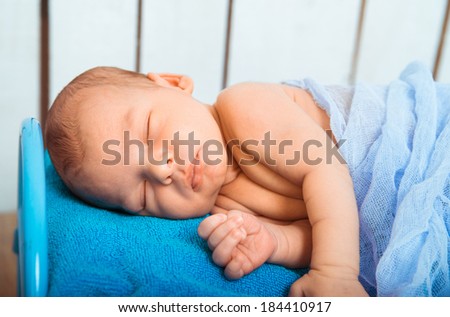 Cute newborn baby sleeps in a small bed with teddy bear