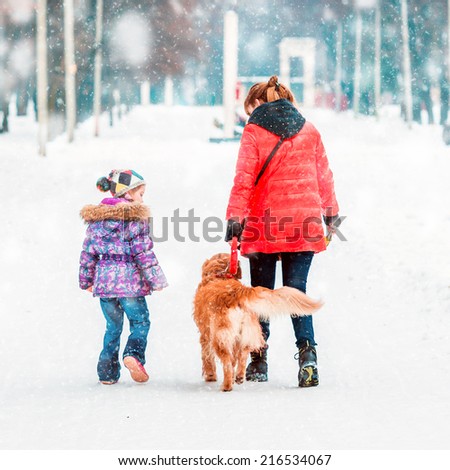 mum with a daughter and their dog walking in winter park