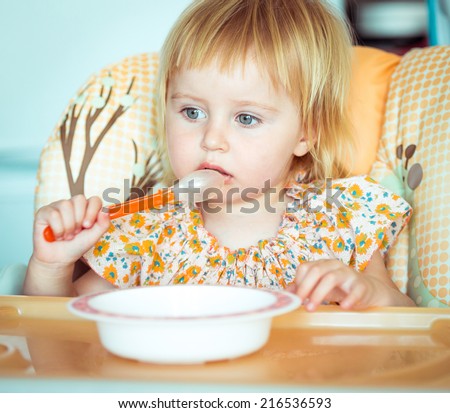 cute baby girl is holding a spoon and going to eat