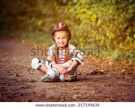 happy little girl sitting on roller skates in the forest