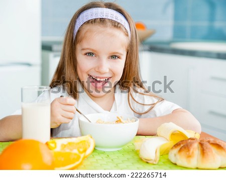 cute little girl eating cereal with the milk in the kitchen
