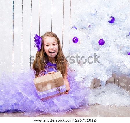smiling little girl with a gift in hands near white Christmas tree