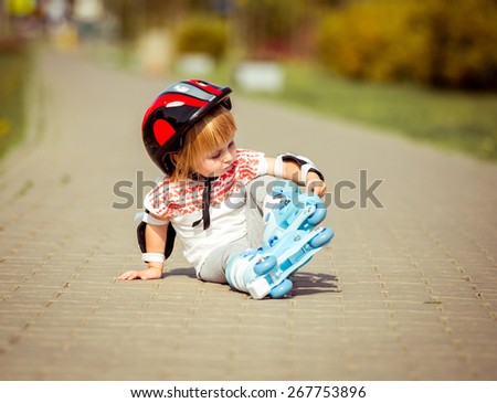 two year old pretty girl in roller skates and a helmet sitting on the street