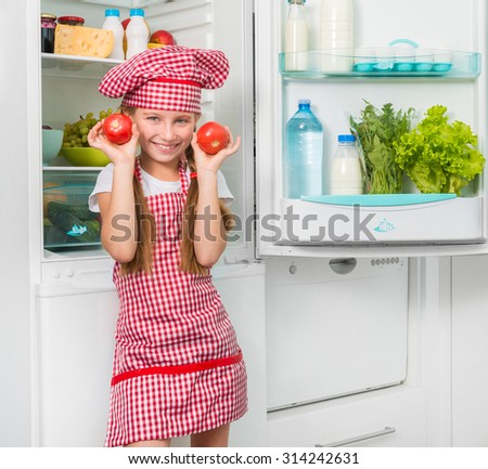 little cook girl holdin tomatoes like eyes near opened fridge