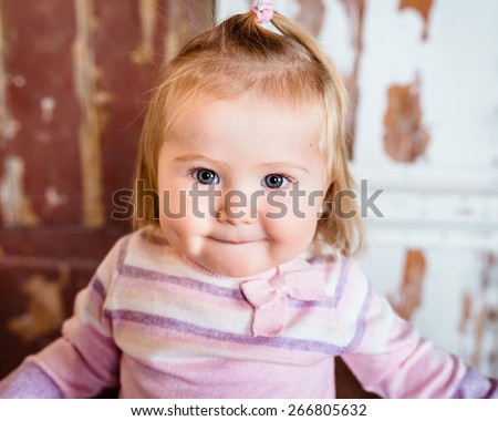 Close-up portrait of funny blond little girl with big grey eyes and plump cheeks with pursed lips. Studio portrait on grunge background