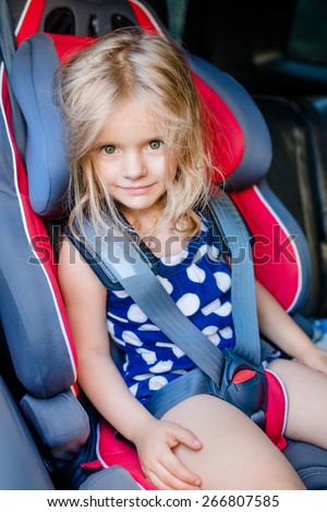 Adorable smiling little girl with long blond hair buckled in car seat looking through the car window