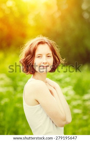 Outdoor portrait of beautiful young woman who hugging herself at summer sunset. Orange and yellow natural toning, golden sunshine