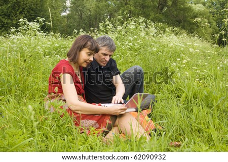 Young couple man and woman with notebook computer in park on green grass.