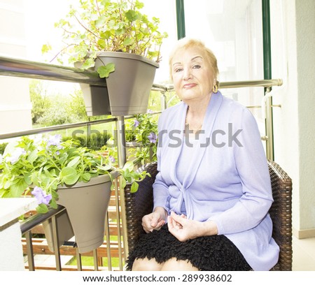 Elderly European blond lady sitting on balcony with flowers.